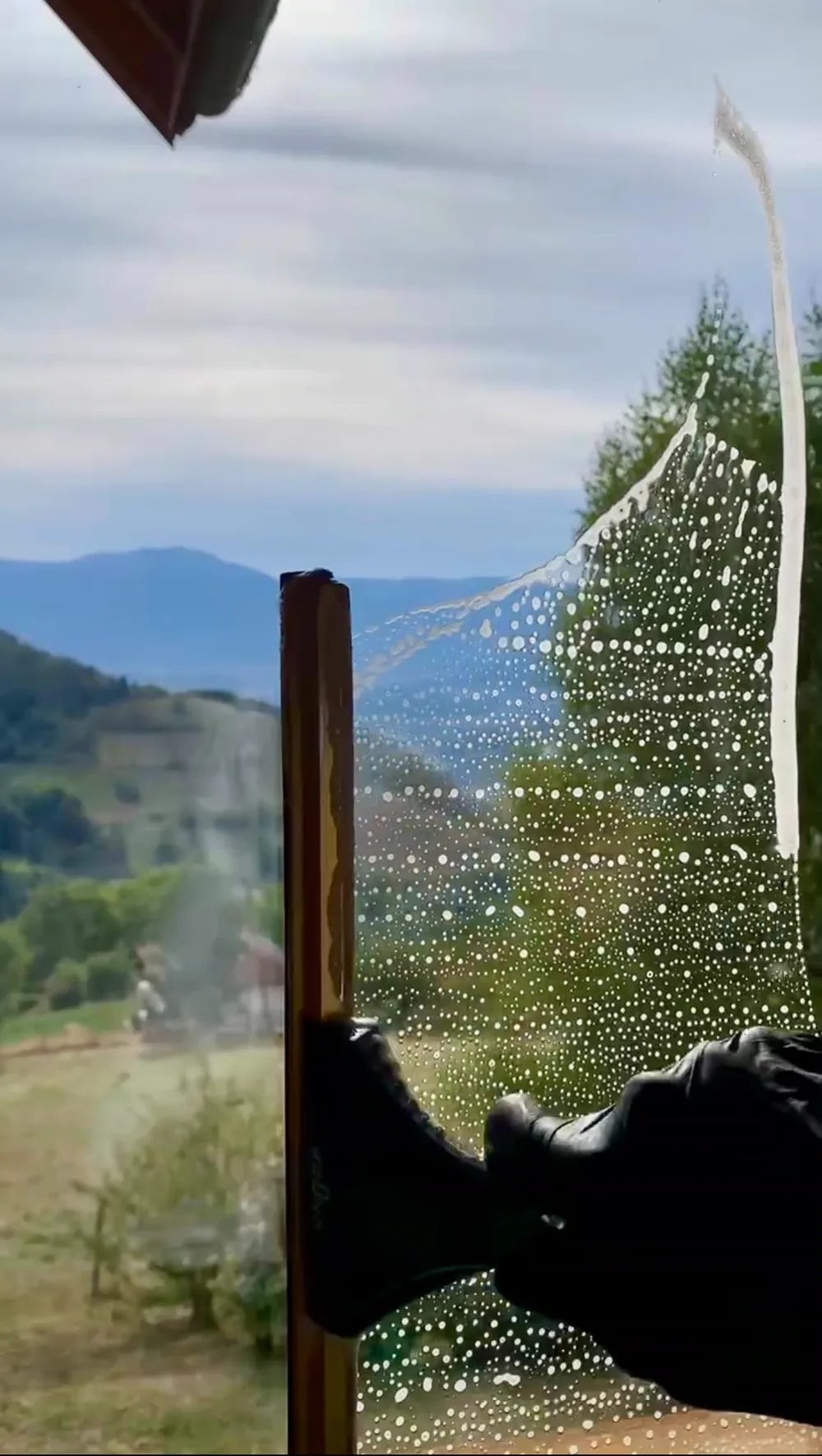 Raclette professionnelle en action sur une vitre savonnée face aux montagnes